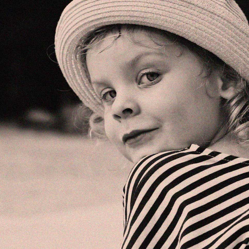 Child in striped shirt and hat smiling.